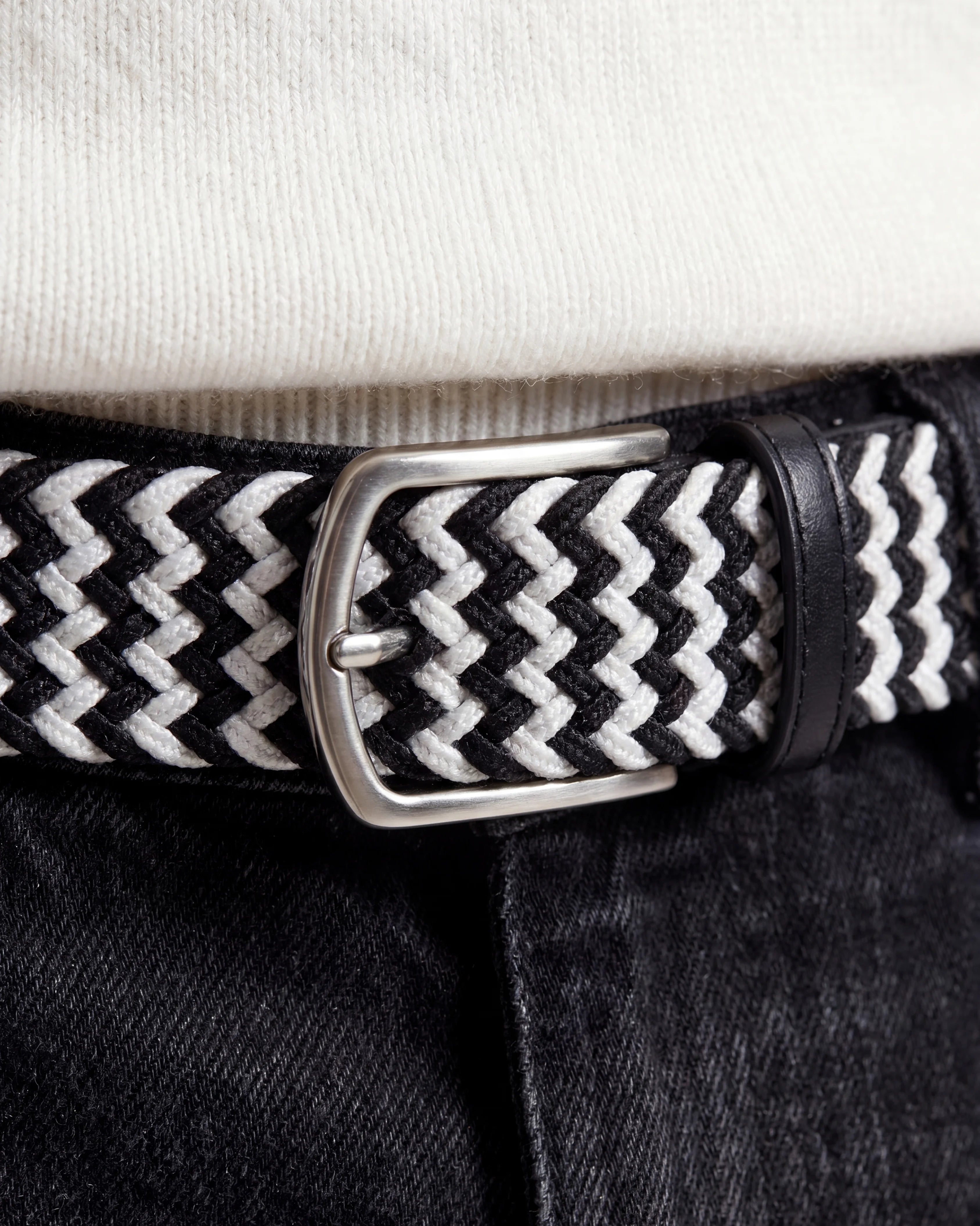 Detaljbild på flätat bälte svart & vit tillsammans med jeans
